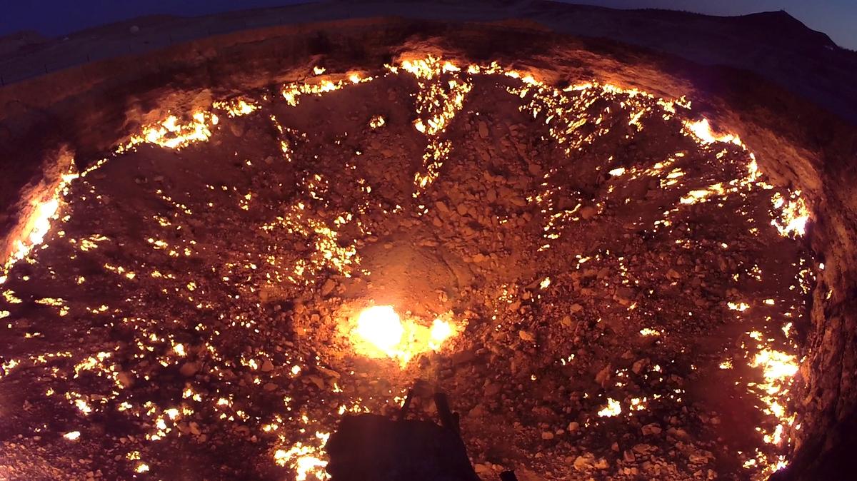The Darvaza Gas Crater, a wide, rocky pit glowing with countless flames at night.