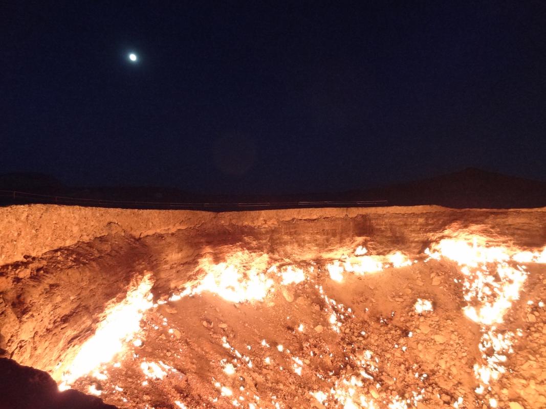 The Darvaza Gas Crater blazes with fire at night beneath a bright moon.