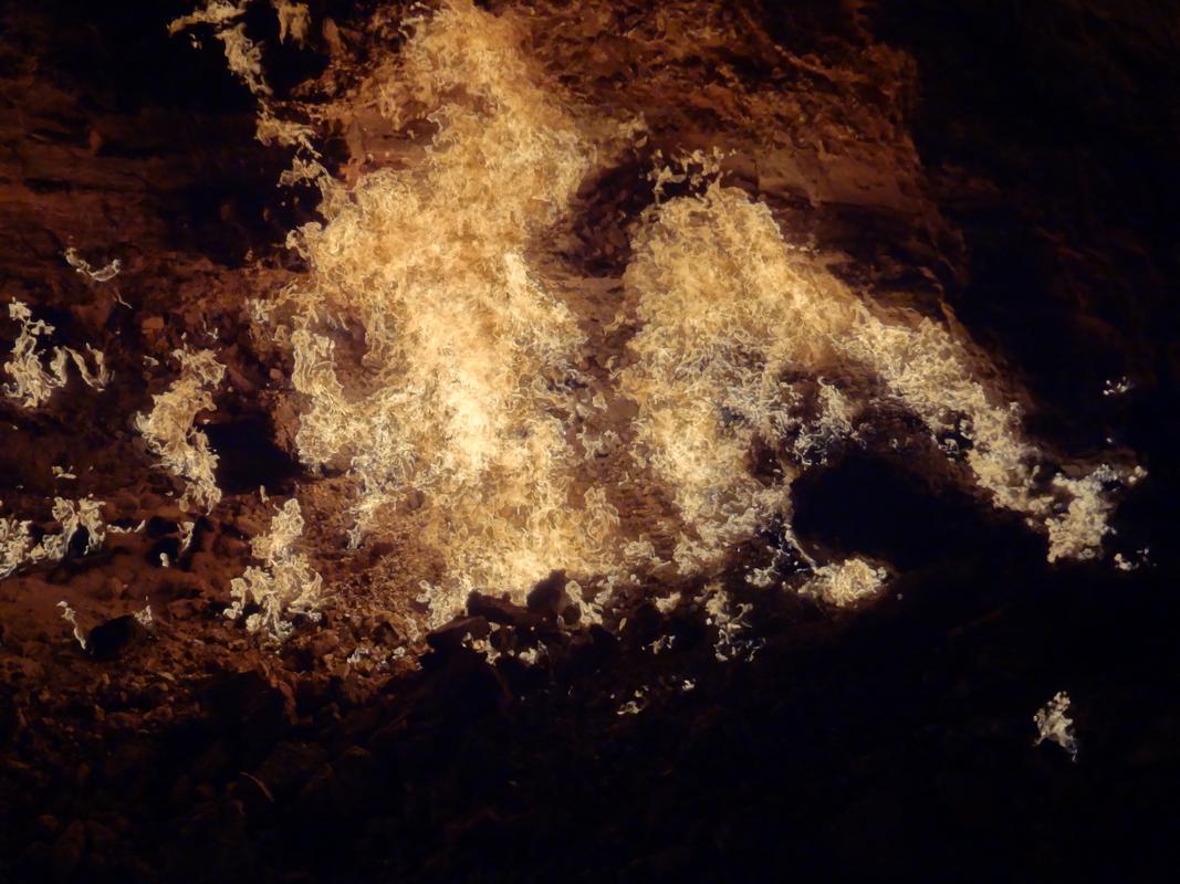 Intense flames burn across the dark, rocky ground of the Darvaza Gas Crater.