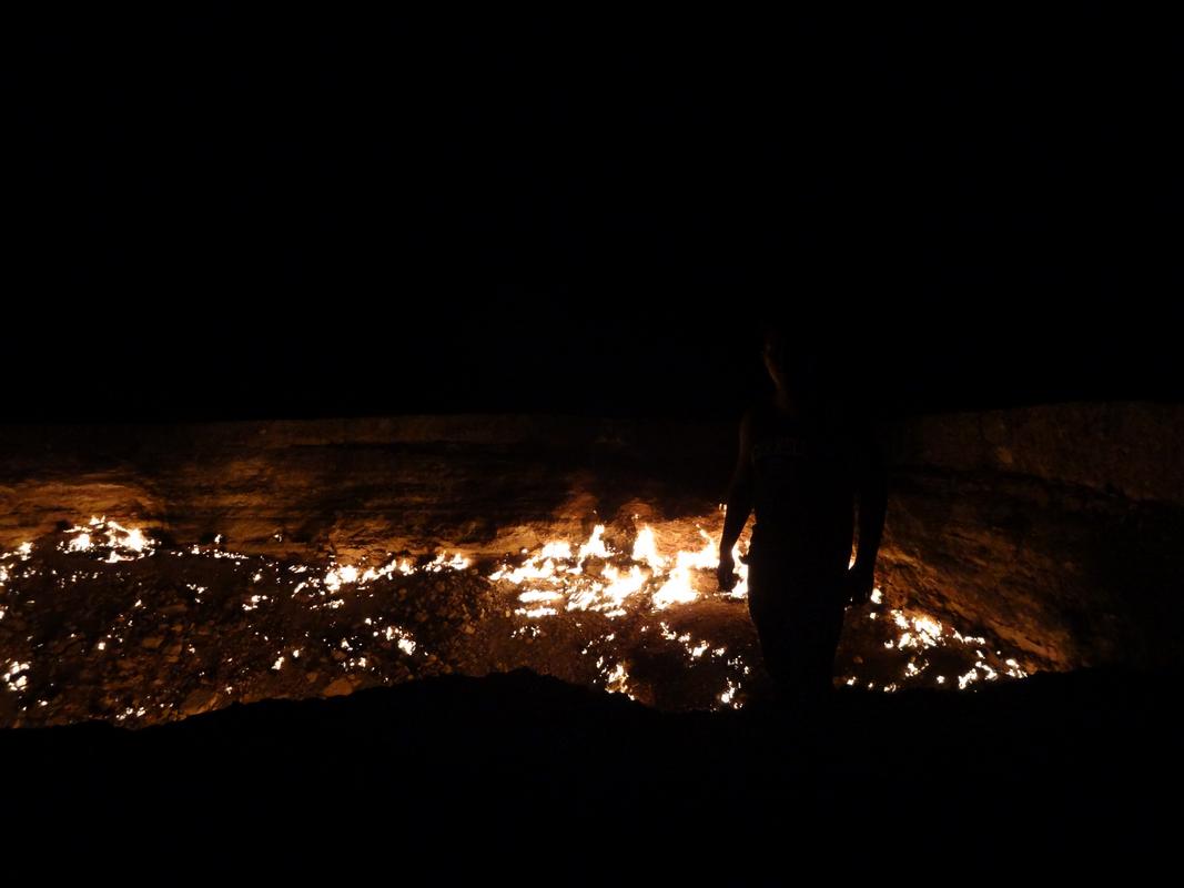 A silhouetted person overlooks the fiery Darvaza Gas Crater at night.