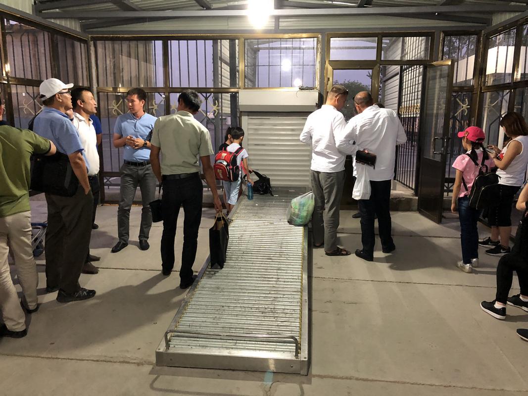 A group of people and a child stand in a waiting area with a metal roller ramp.