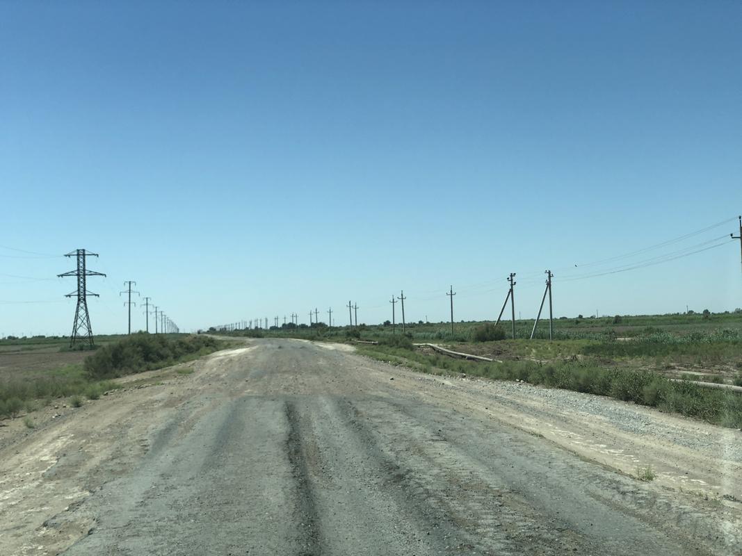 A long, unpaved road stretches into the distance, lined with utility poles under a clear blue sky.