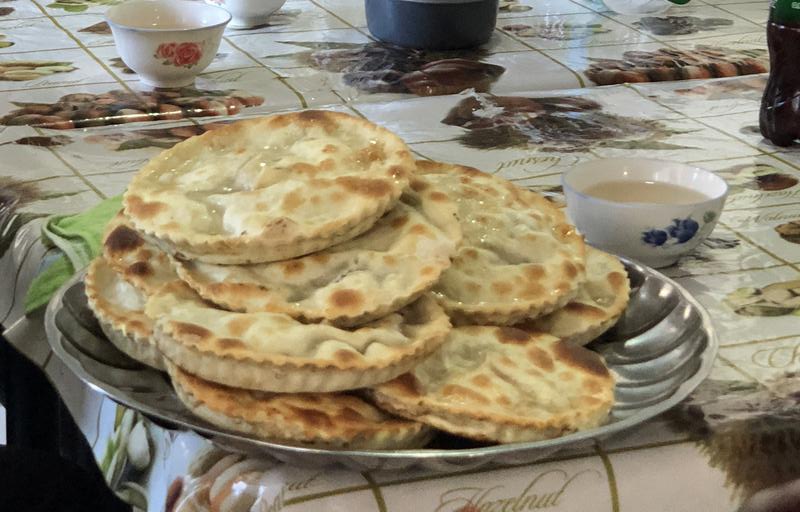 A plate piled with golden-brown round flatbreads sits on a patterned tablecloth, with small bowls in the background.