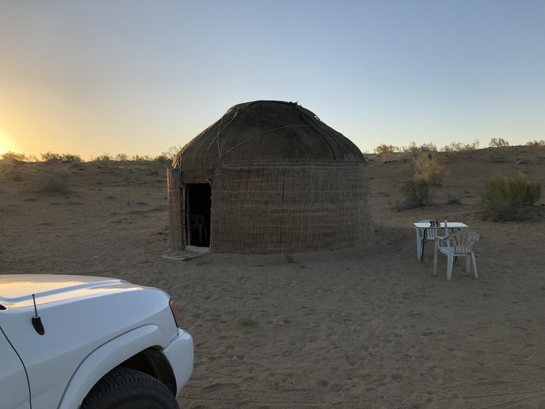 A traditional yurt, white SUV, and outdoor seating in a desert landscape at sunset.