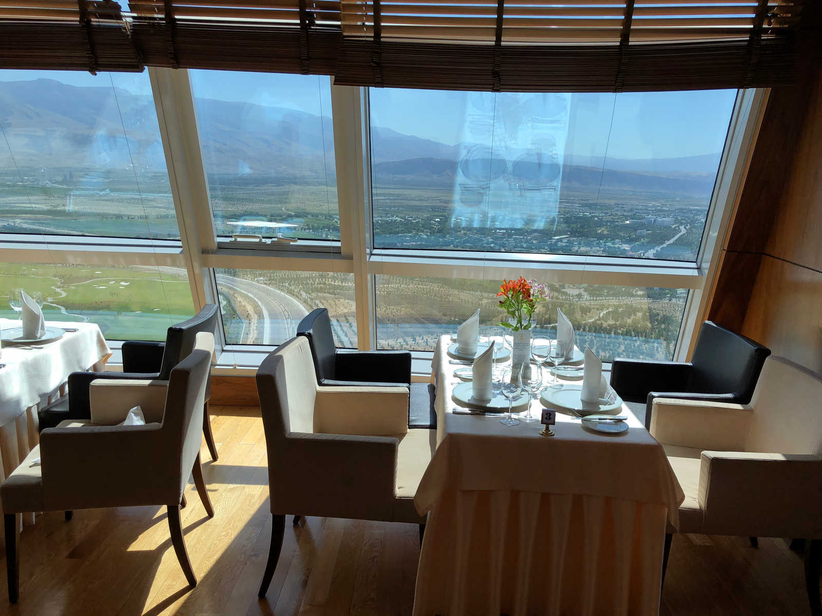 An elegant restaurant dining room with set tables and panoramic views of mountains and the landscape from large windows.
