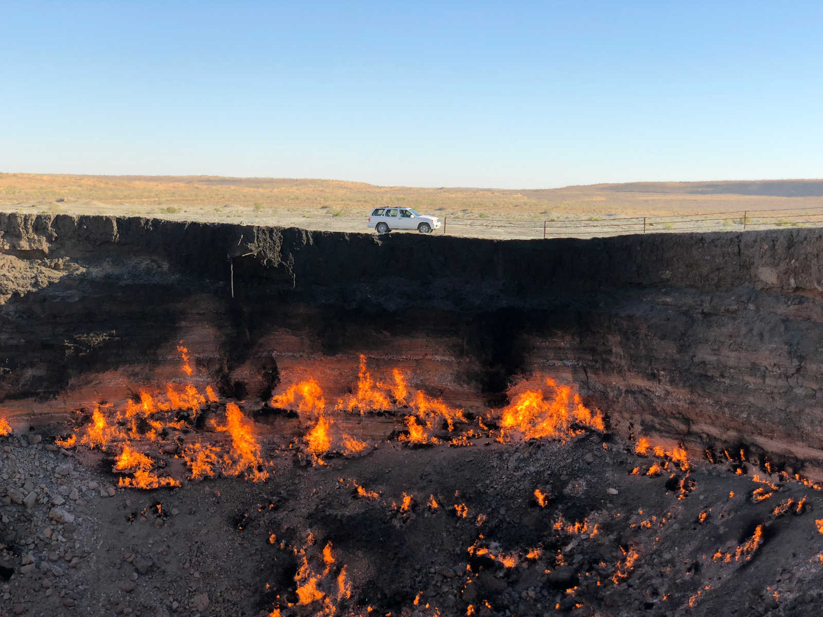 A white SUV sits on the edge of a fiery crater in a barren desert landscape.