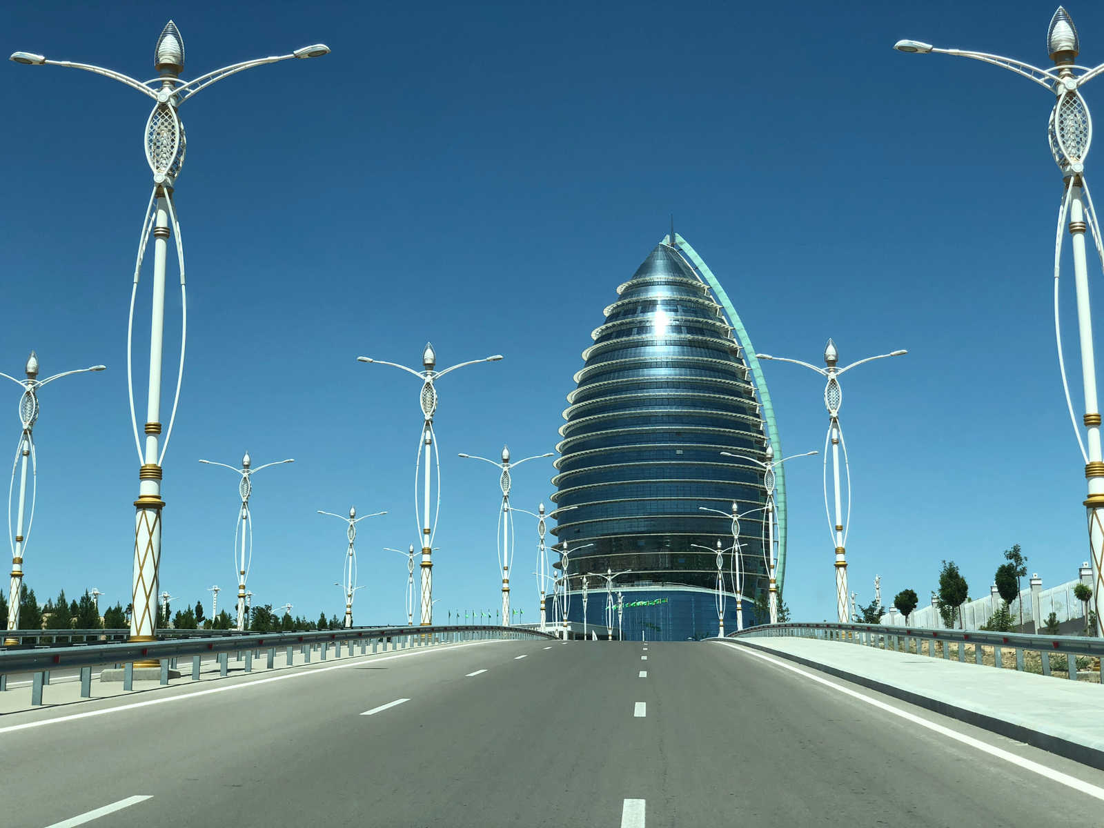 The modern, egg-shaped Yyldyz Hotel with a spiral glass facade stands at the end of a road lined with elaborate streetlights.