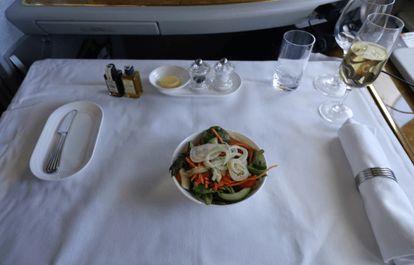 A first class airplane meal with a salad, champagne, and a formal table setting.