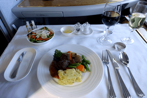 A first-class airplane meal of steak, salad, and wine served on a white tablecloth.