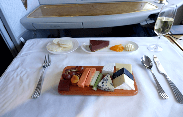 An Emirates First Class meal setting with a cheese board, dessert, crackers, and champagne on a white tablecloth.