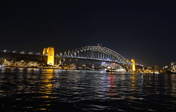 Sydney Harbour Bridge illuminated at night with reflections on the water.