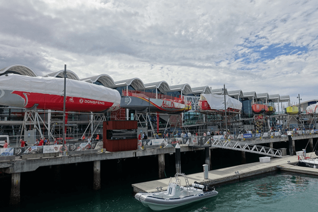Volvo Ocean Race yachts on stands along a bustling waterfront in Auckland.