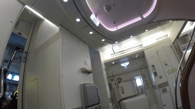The well-lit interior of an Emirates A380 aircraft entryway with a partial view of the cockpit.