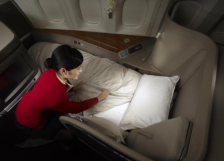 A Cathay Pacific flight attendant makes a bed in a luxurious first-class airplane suite.