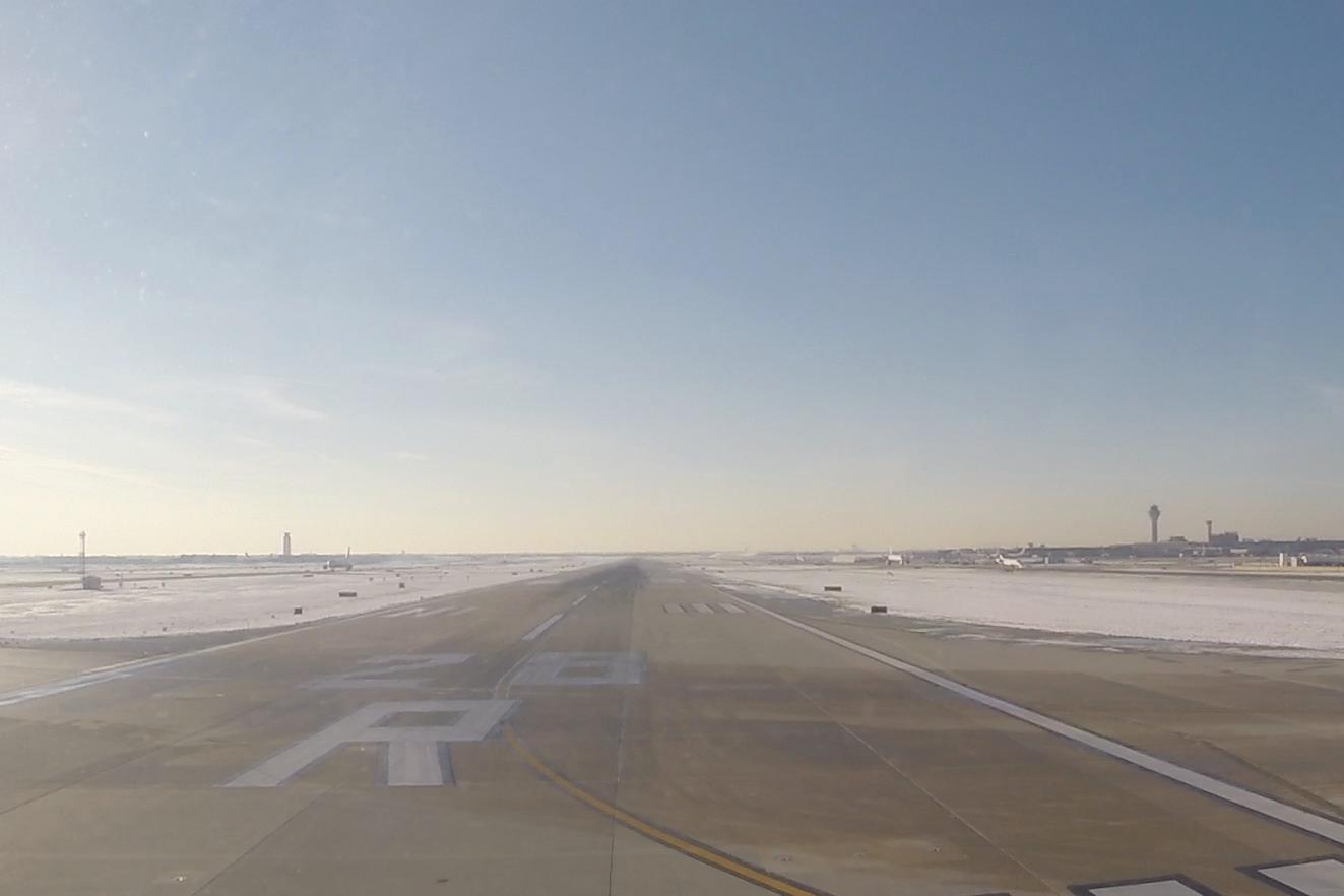 View from an airplane window showing a snowy airport runway with a distant control tower under a clear sky.