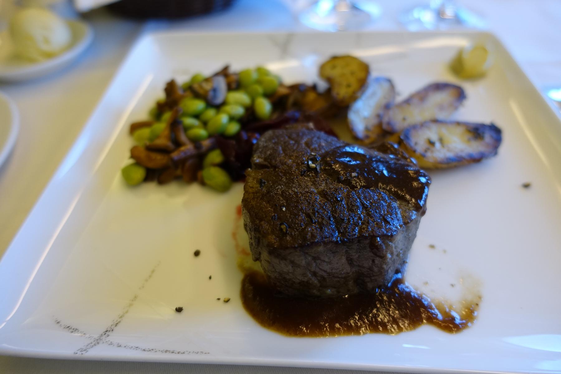 A first class meal of steak with sauce, edamame, and roasted potatoes on a white plate.
