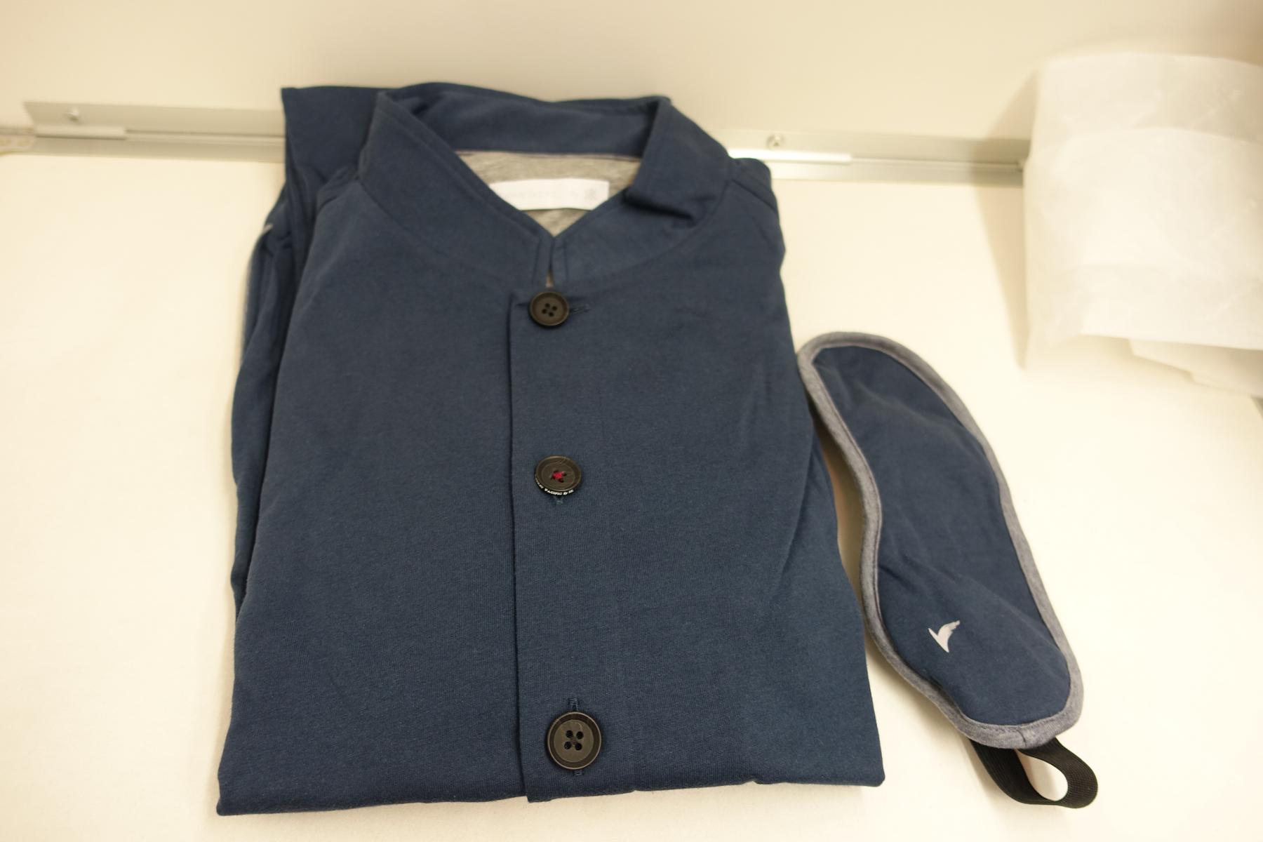 A folded dark blue Cathay Pacific First Class pajama top and a matching eye mask with a bird logo.