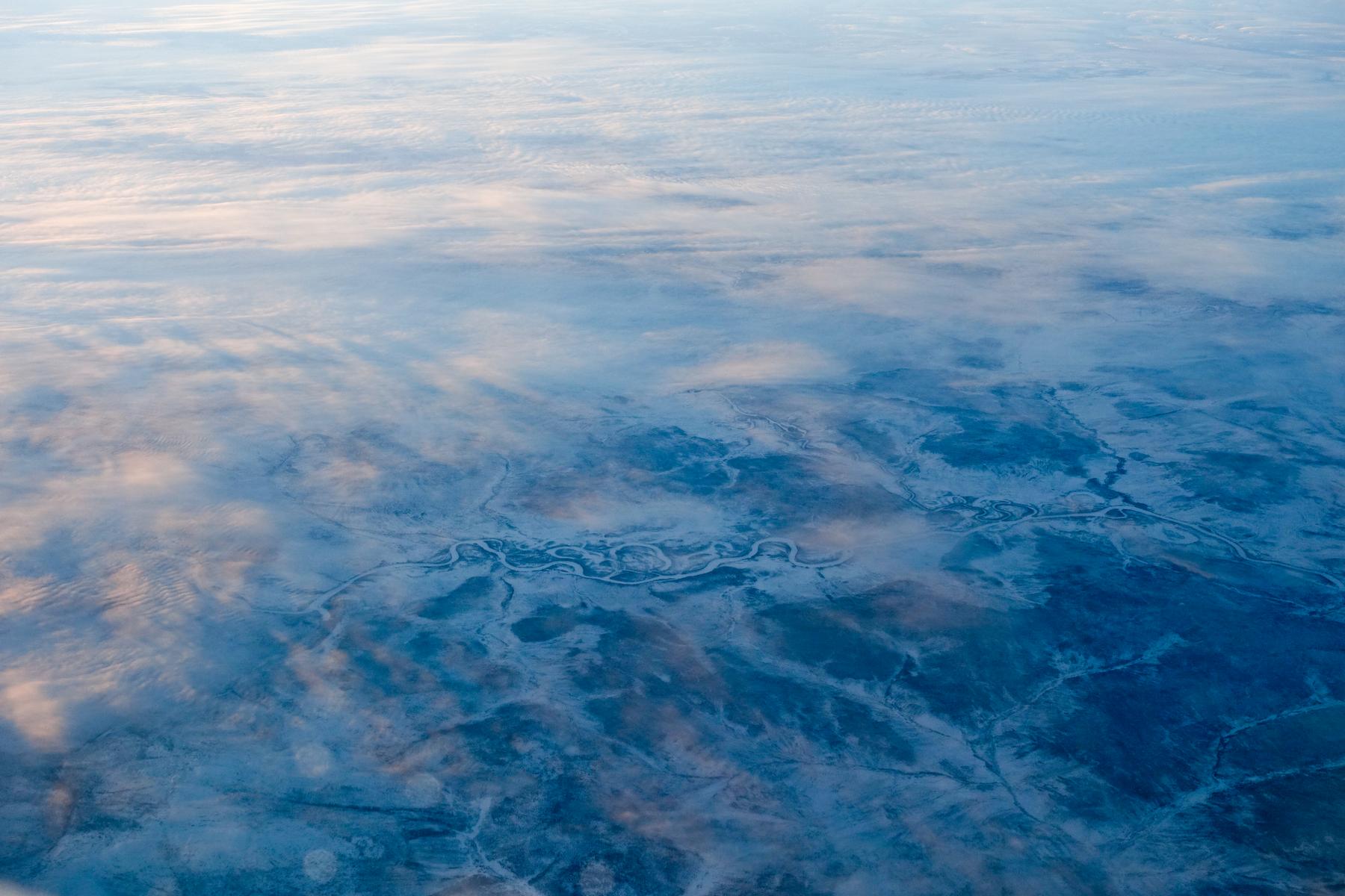 Aerial view of a vast icy landscape featuring winding rivers and scattered clouds.