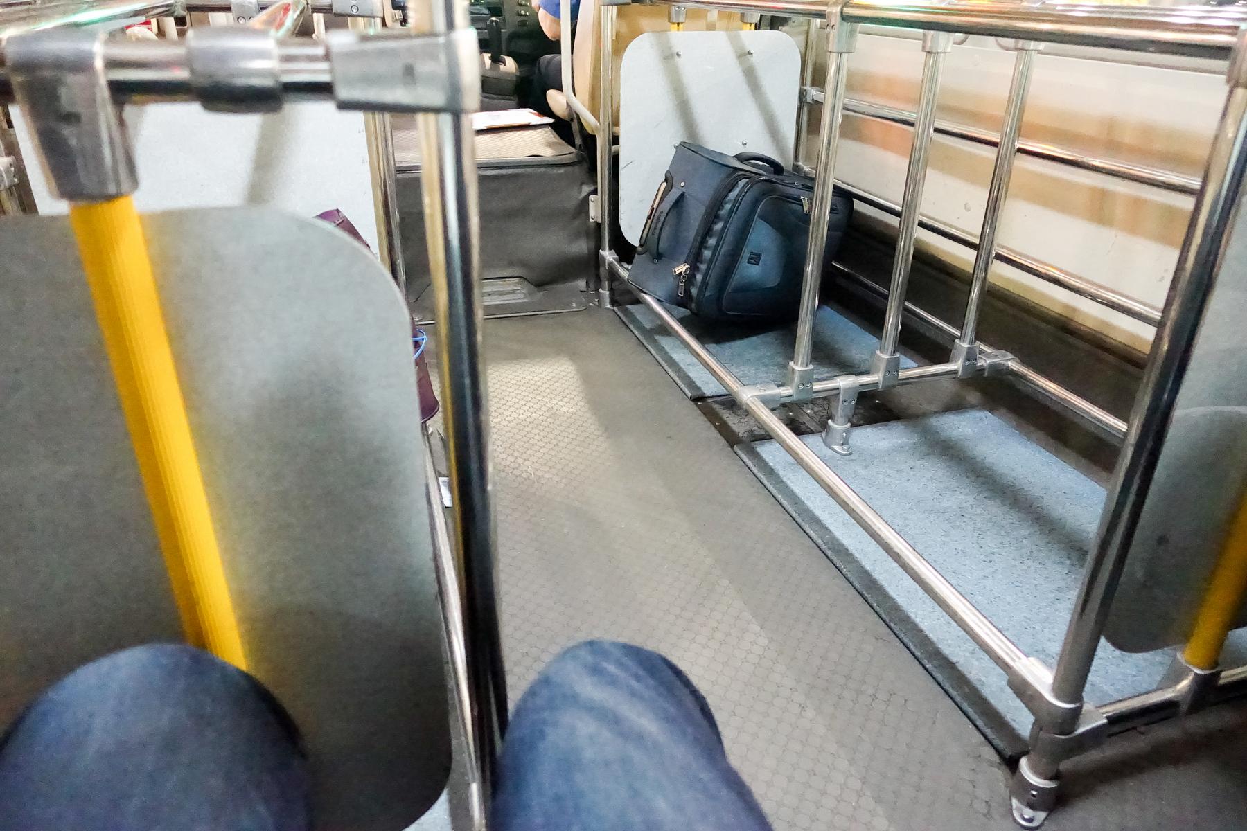 A person's legs are visible inside a bus or train, with a black bag on the floor.