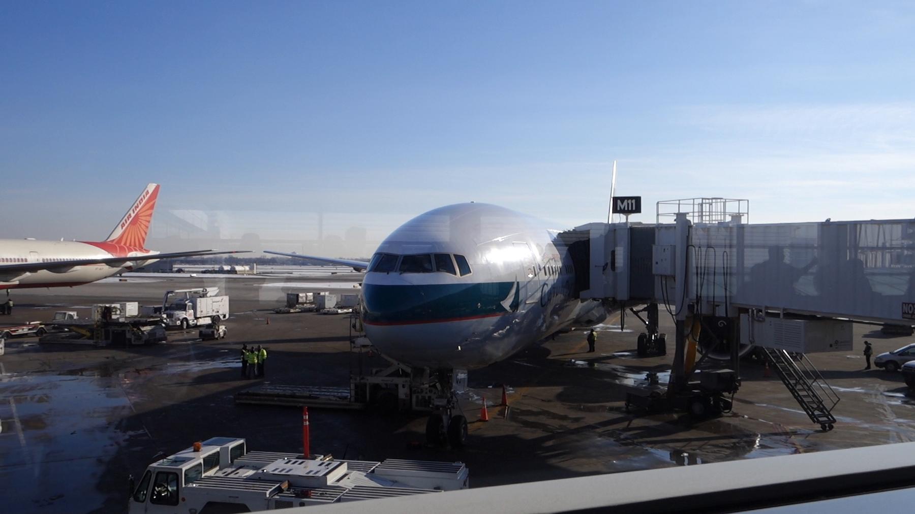 A Cathay Pacific plane at an airport gate with an Air India plane in the background.