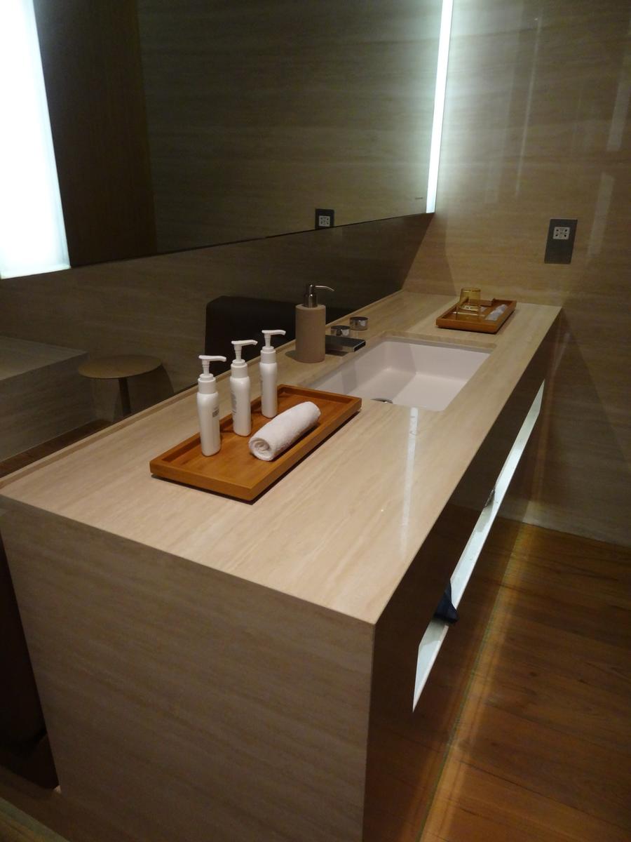 An elegant stone bathroom vanity with a sink, toiletries, and a rolled towel on a wooden tray.