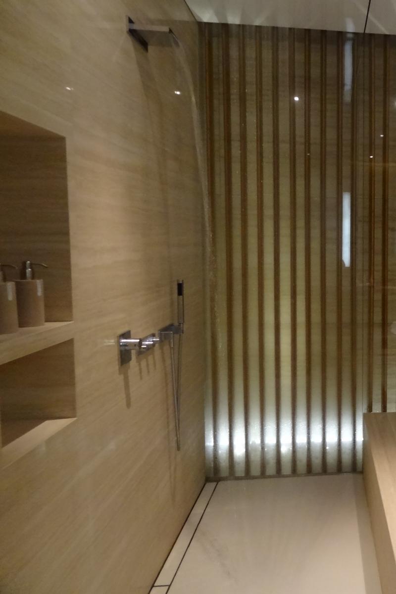 A modern shower room with a running waterfall shower, light-toned walls, and an illuminated slatted accent wall.