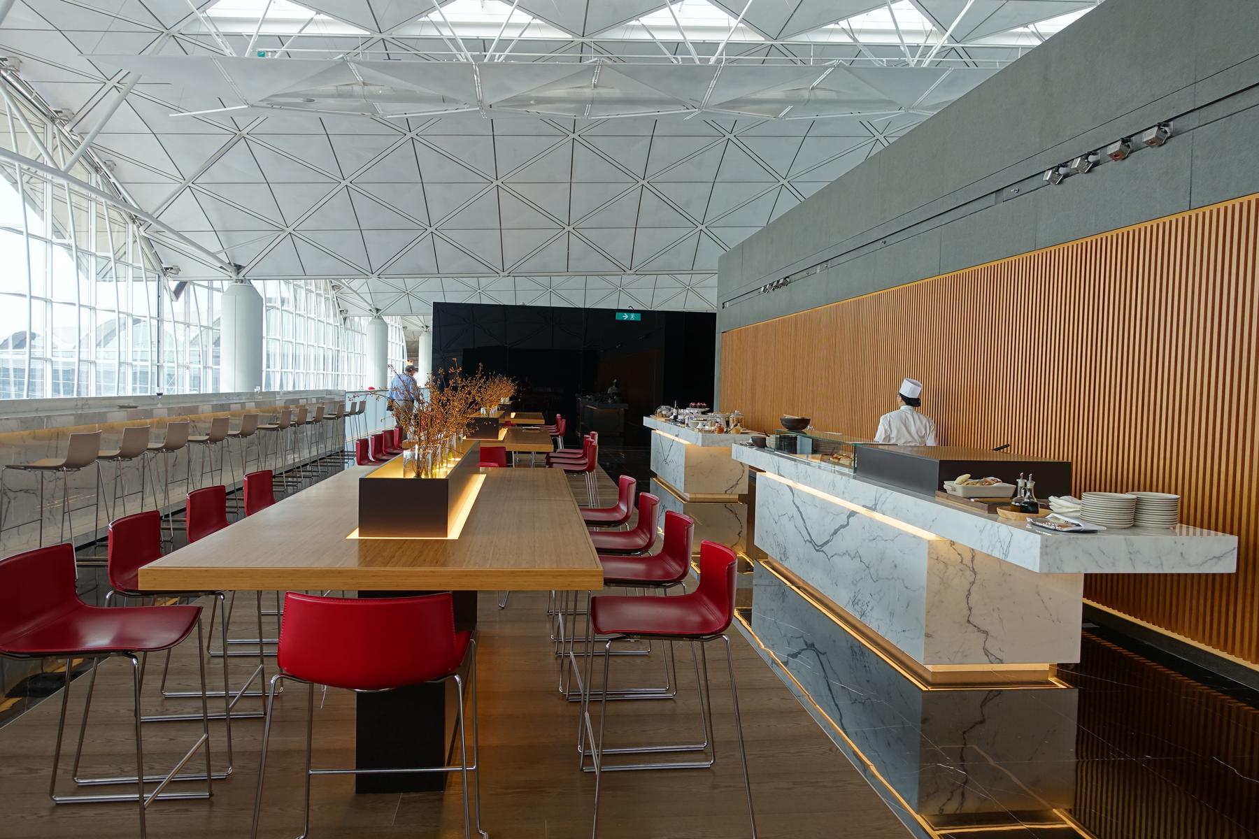 Inside a bright Cathay First Class Lounge with a chef at a marble food bar and extensive seating.
