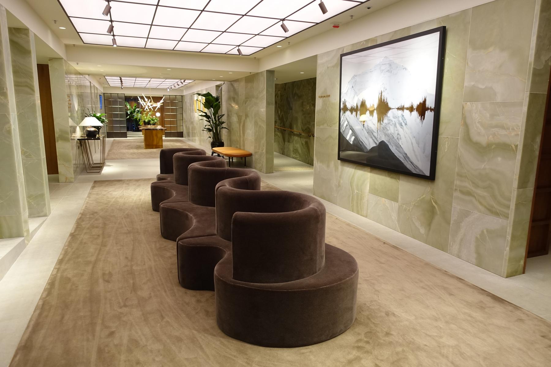 A luxurious first-class lounge hallway features a long, wavy brown velvet sofa, green marble walls, and a large abstract mountain artwork.