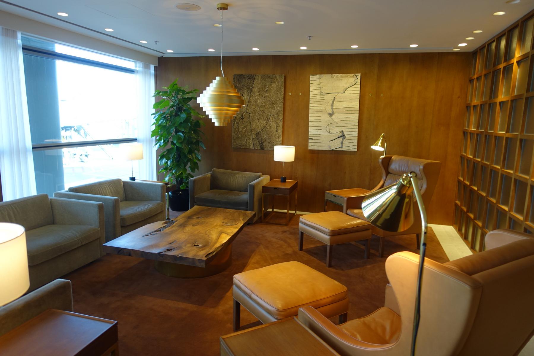 A stylish lounge area with tan and grey seating, wooden walls, a large window, and modern decor.