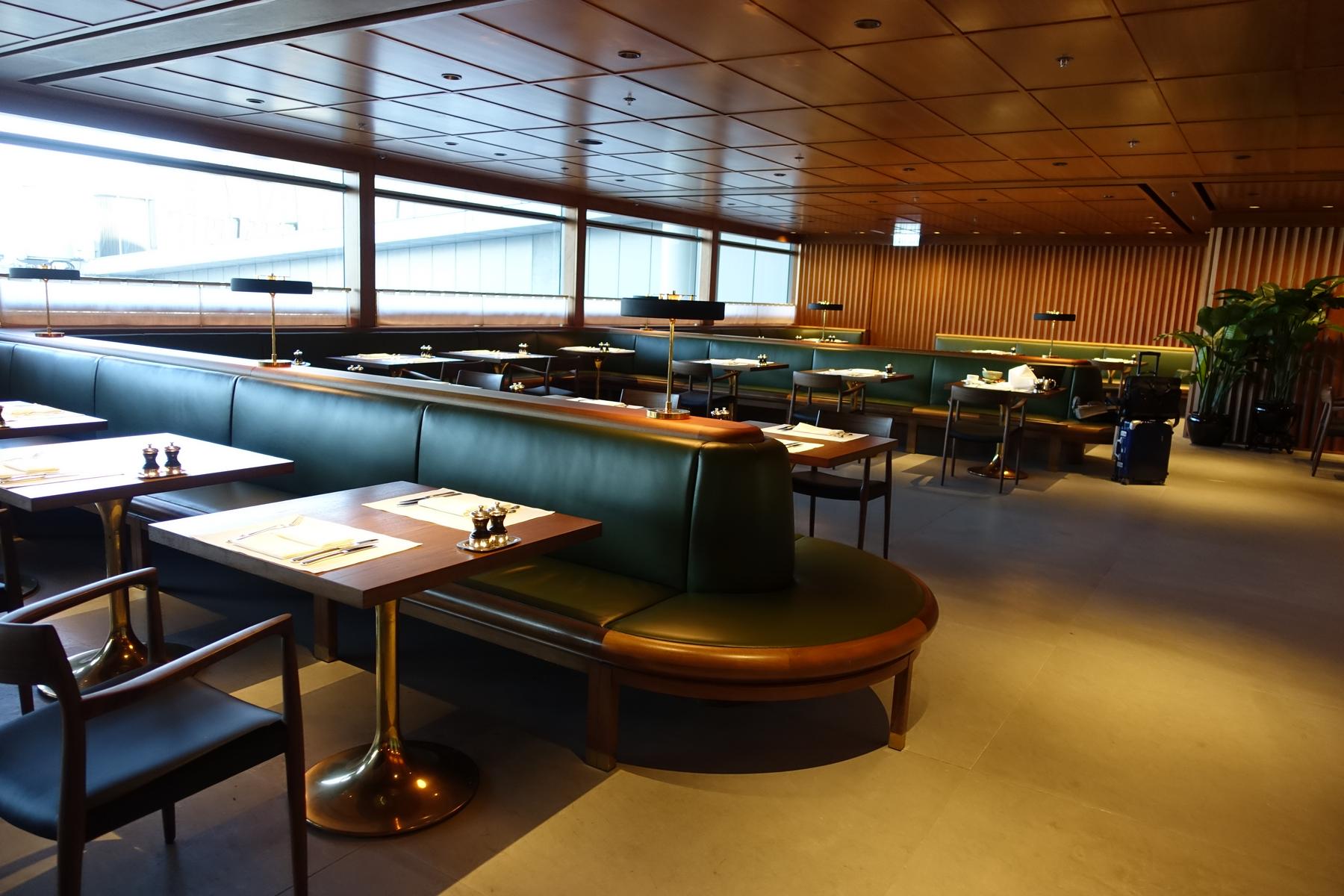 An elegant lounge dining room with long dark green leather booths, wooden tables, and large windows.