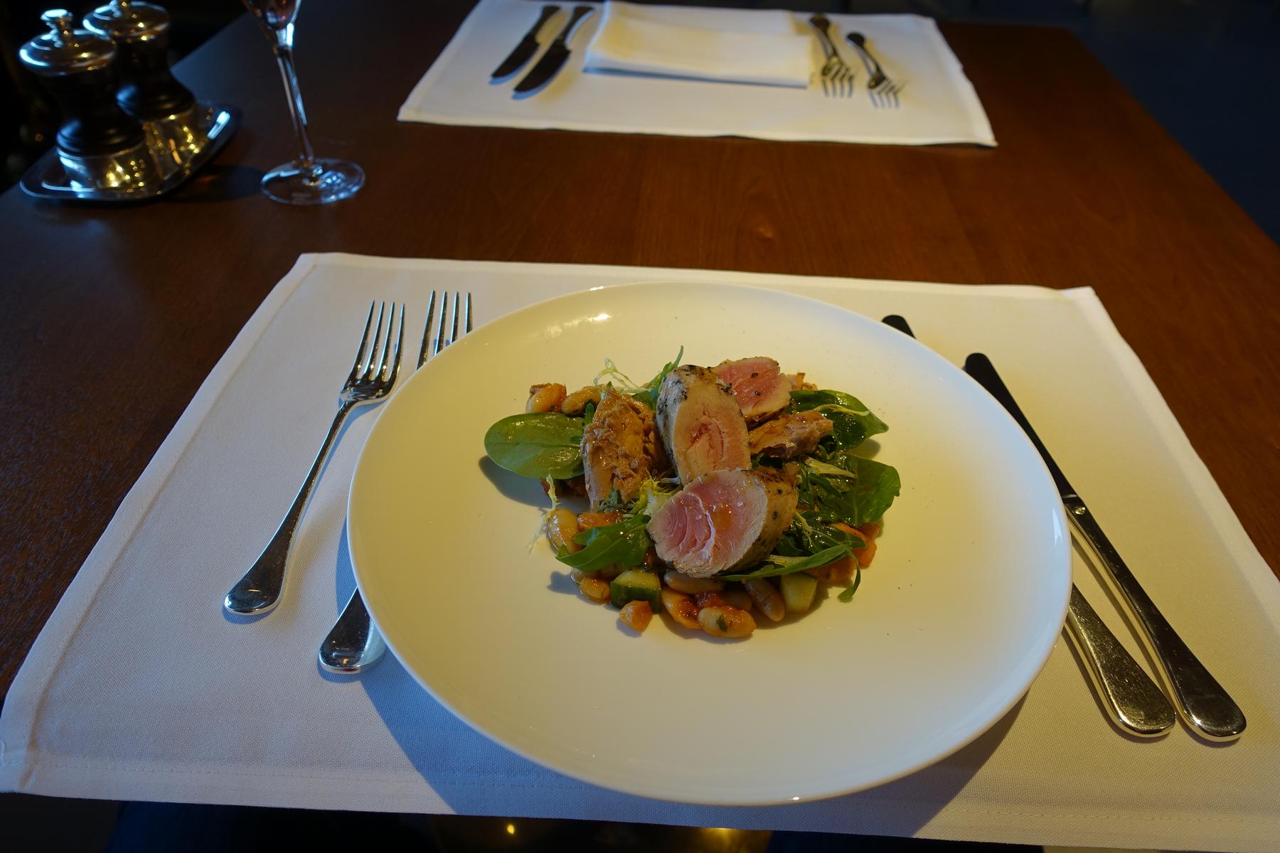 A white plate of seared tuna with greens and beans sits on a wooden dining table.