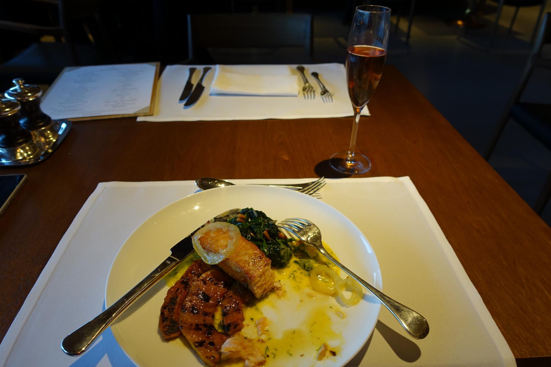 A partially eaten salmon and vegetable dish with a glass of rosé champagne on a wooden dining table.