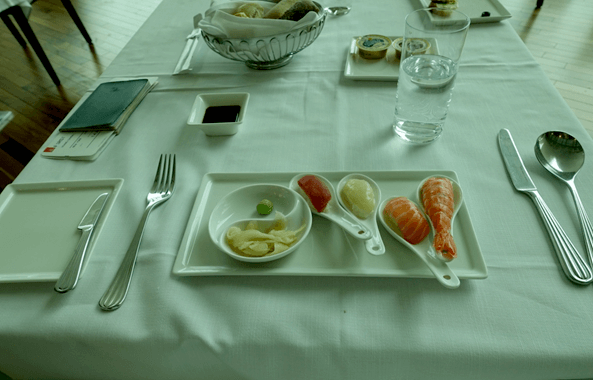 An Emirates First Class meal setting with sushi components, bread, and a glass of water.