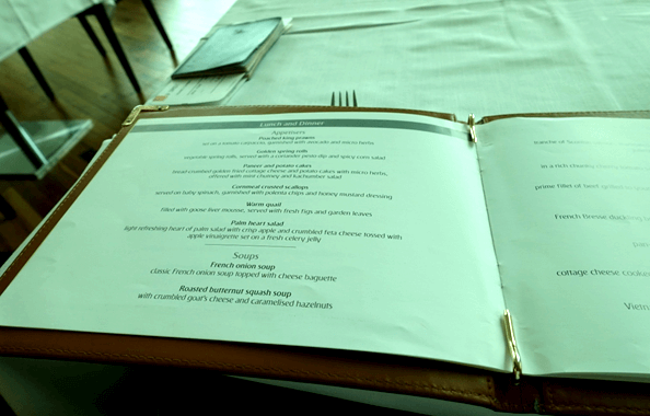 An open Emirates First Class menu displays a list of appetizers and soups on a white tablecloth.