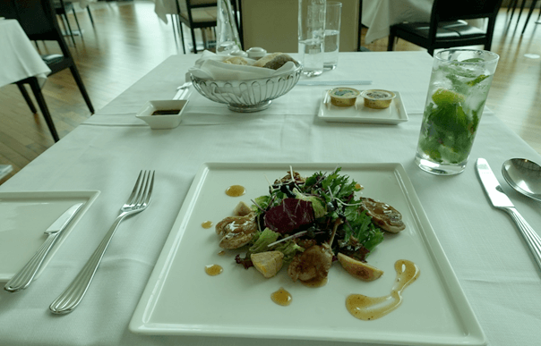 A white-linened table set with a plated salad, bread basket, and a mint beverage.