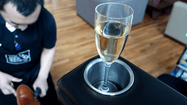 Champagne in a first-class seat cup holder with a shoe shiner in the background.