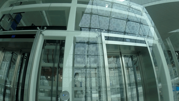 Glass elevators in a bright, modern airport terminal featuring patterned glass walls.