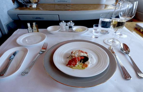 An elegant seafood meal with champagne served on a white tablecloth in Emirates First Class.