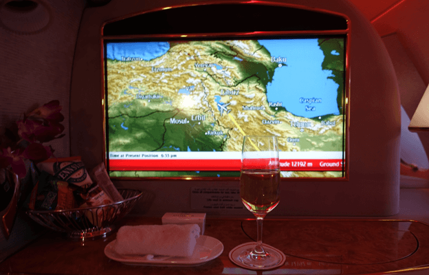 Emirates First Class suite with a flight map on screen, champagne, and snacks.