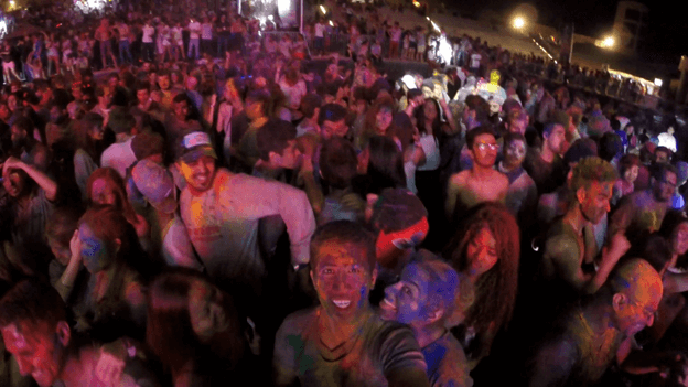 A large crowd of people covered in colorful powder at a vibrant nighttime festival.