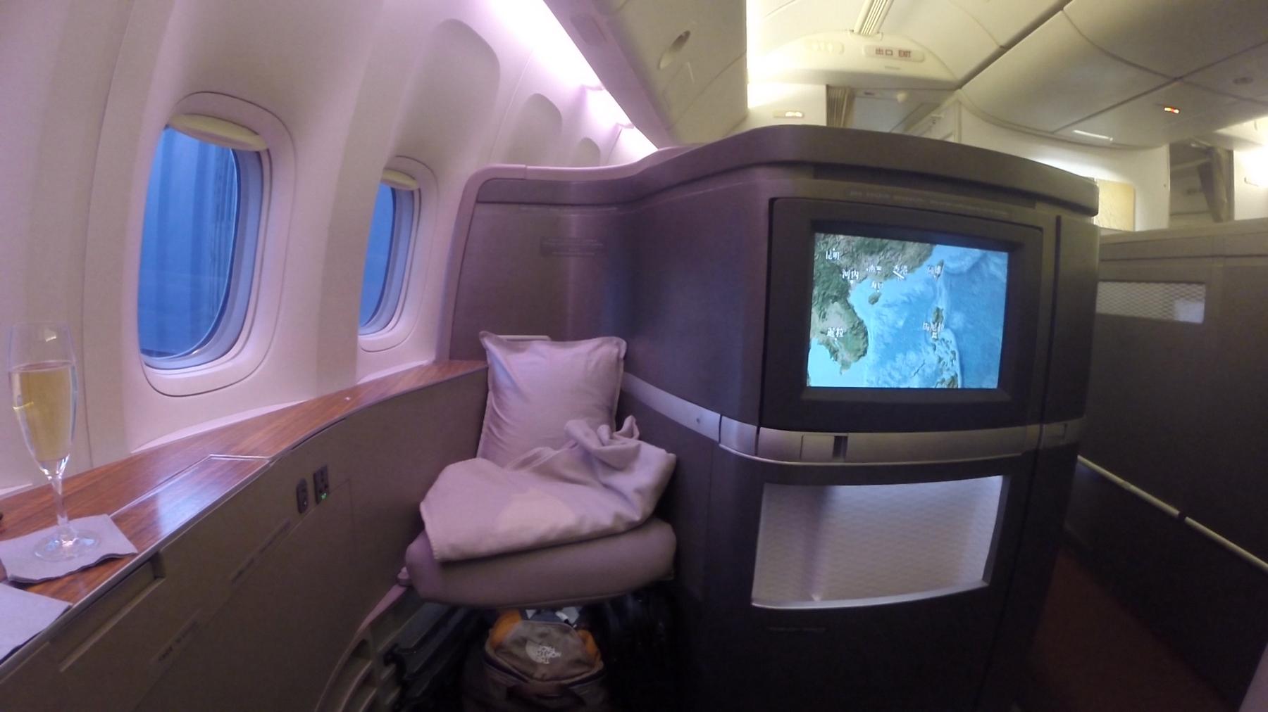 A Cathay Pacific First Class suite featuring a glass of champagne, a comfortable seat, and a flight map displayed on the monitor.
