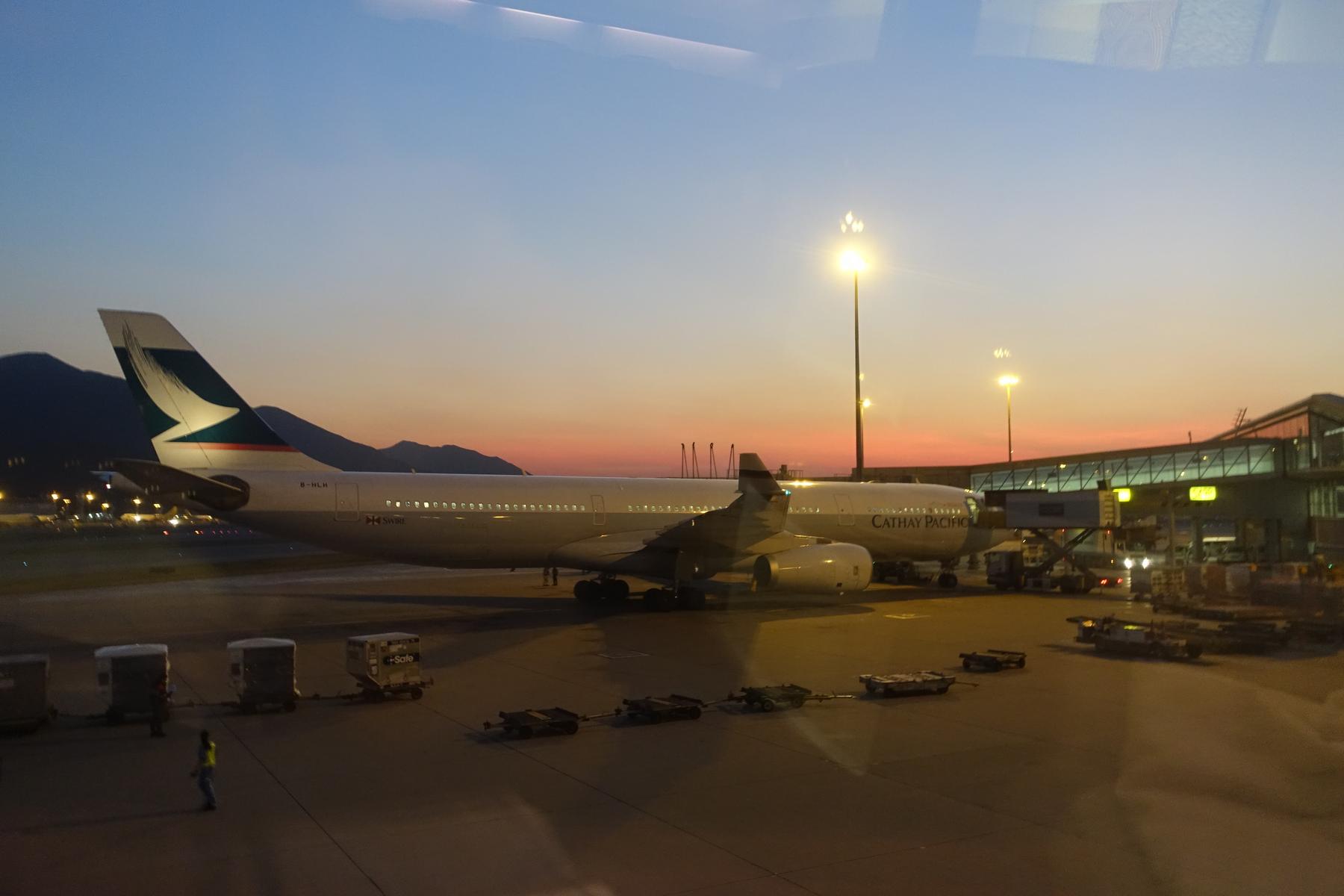 A Cathay Pacific airplane parked at an airport gate during sunset.