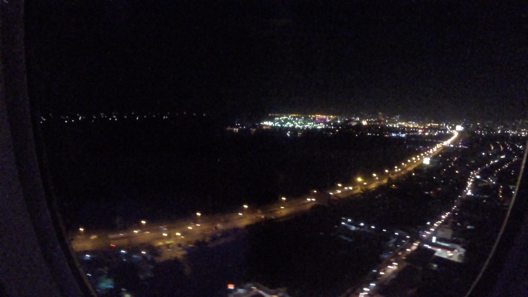 An aerial night view of city lights, with brightly lit roads and clusters of buildings.