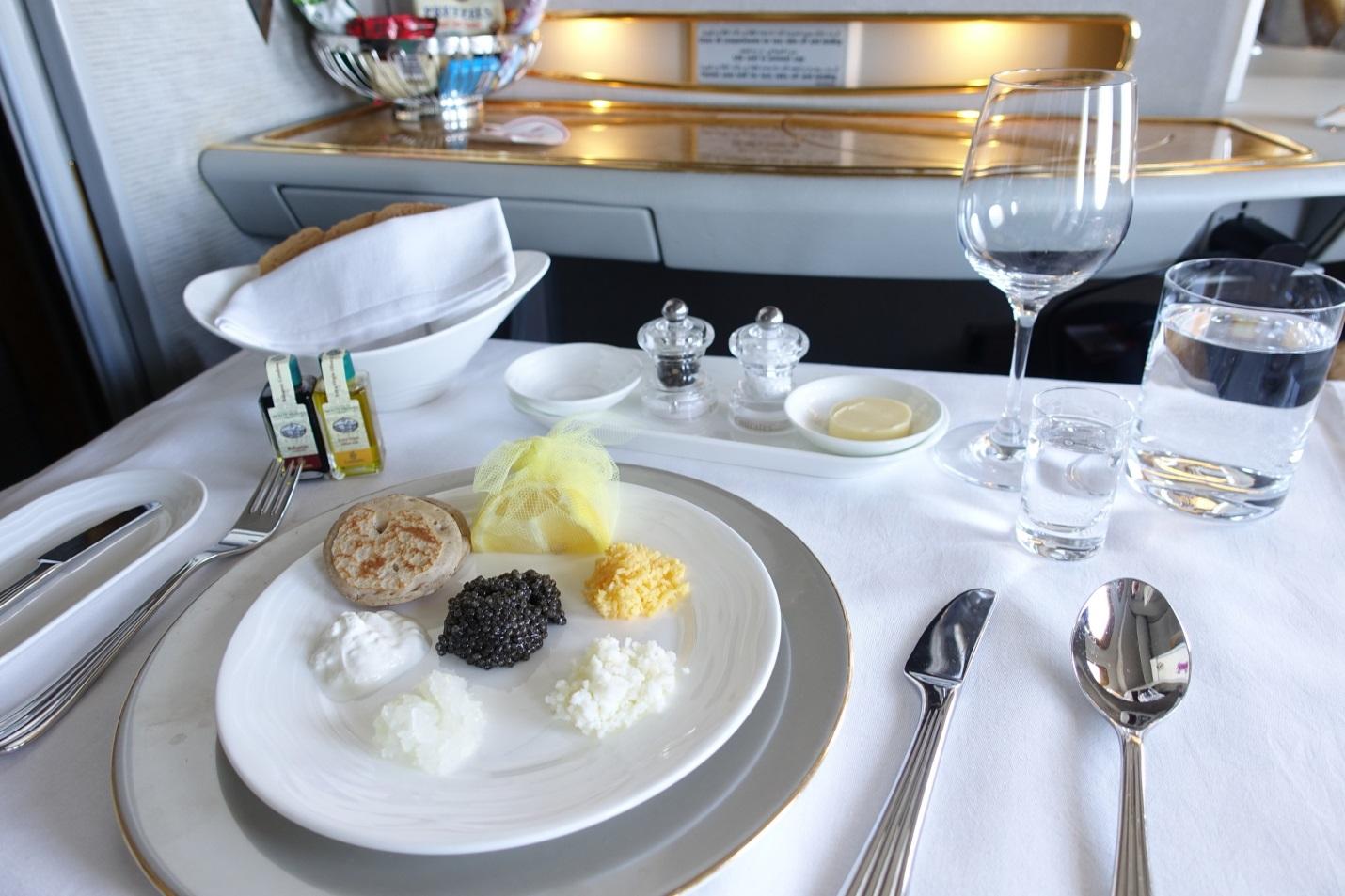 A plate of caviar and blinis with accompaniments served on a table in an Emirates First Class cabin.