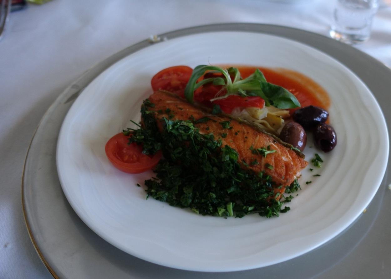 Emirates First Class meal: a salmon fillet garnished with herbs, cherry tomatoes, and olives.