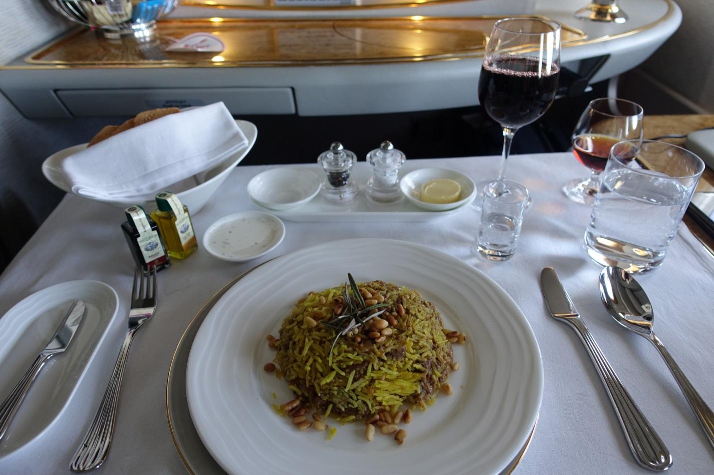 Emirates First Class meal service with a plate of rice, bread, wine, and a complete table setting.