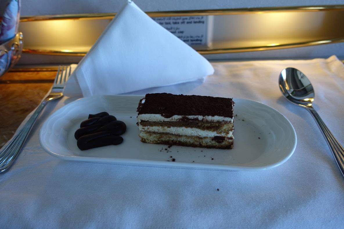 Tiramisu and chocolate garnishes on a plate with cutlery in Emirates First Class.