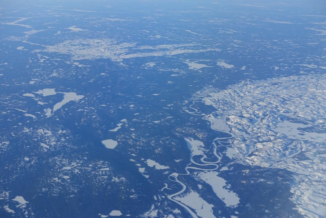 Aerial view of a vast, snow-covered landscape with a winding river and frozen lakes.