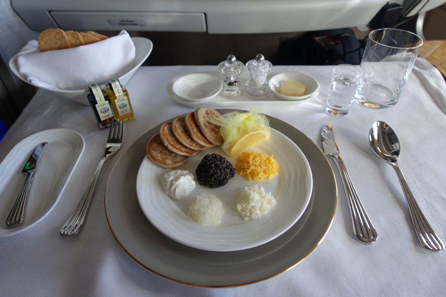 Emirates First Class caviar service featuring blinis, black caviar, and various garnishes, set on a tray table.