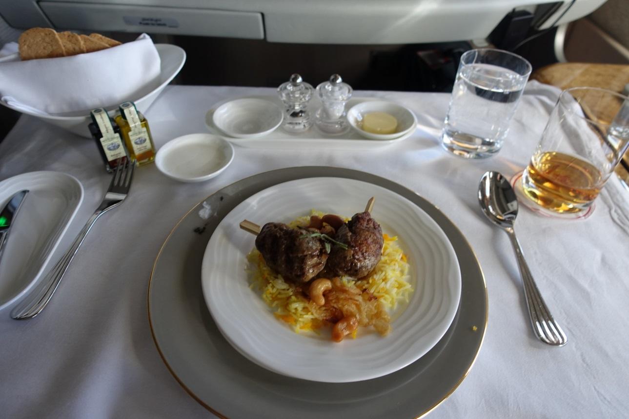 An Emirates First Class airplane meal featuring meat skewers with rice, bread, and drinks.